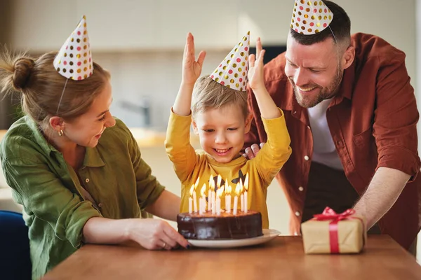 小さな男の子の息子は 若い愛情のある両親と誕生日を祝いながら ケーキの上にろうそくを吹きに行きます お祝いを受けながら 興奮した子供は腕を上げて笑顔と家族からプレゼント — ストック写真