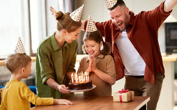 興奮した女の子はチョコレートケーキの上にろうそくを吹き 家で幸せな家族と彼女の誕生日を祝いながら願いを作ります パーティー帽子の正の両親お祝いの娘 — ストック写真