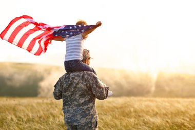 Amerikan bayrağını omuzlarında taşıyan ve güneşli bir günde harika yaz manzarasının tadını çıkaran mutlu bir baba, mutlu bir erkek asker, Amerikan ordusundan sonra oğluyla bir araya geldi.