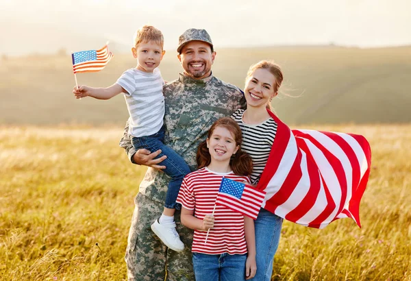 Military homecoming. Young military man soldier happy to be reunited with his patriotic family, smiling wife and two kids with American flags meeting father from US army while standing in meadow