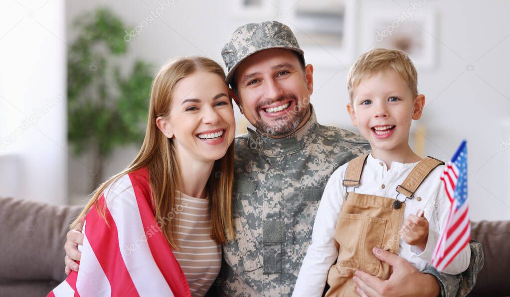 Happy young man father in military uniform reunited with his beautiful american family, hugging with smiling wife and cute kid son with flag of United States in hand, meeting daddy from US army at home