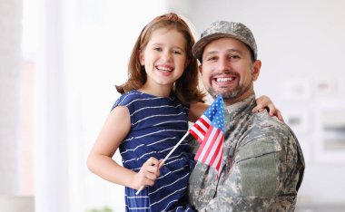 Askeri üniformalı mutlu Amerikan aile babasının portresi ve Amerikan bayrağıyla kucaklaşan ve gülümseyen tatlı küçük kız çocuğu. Erkek asker baba evde ailesiyle bir araya geldi.