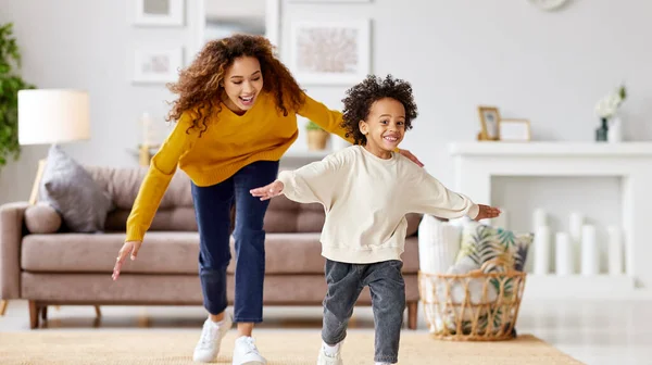 楽しいアフリカ系アメリカ人の母親は 家で一緒に遊んでいる間 興奮した小さな子供の息子を捕まえようとしています 余暇を楽しむ幸せな家族 — ストック写真