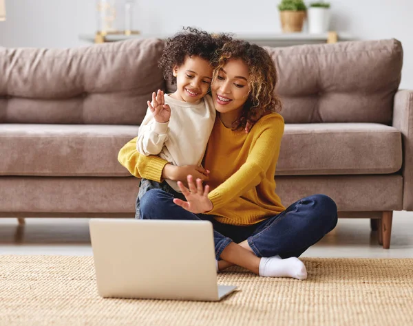 幸せなアフロアメリカの家族若い正の母親とかわいい男の子息子持っているビデオ通話とともに家族のラップトップ コンピュータ画面を見て 手を振っながら一緒にリラックスソファに家 — ストック写真