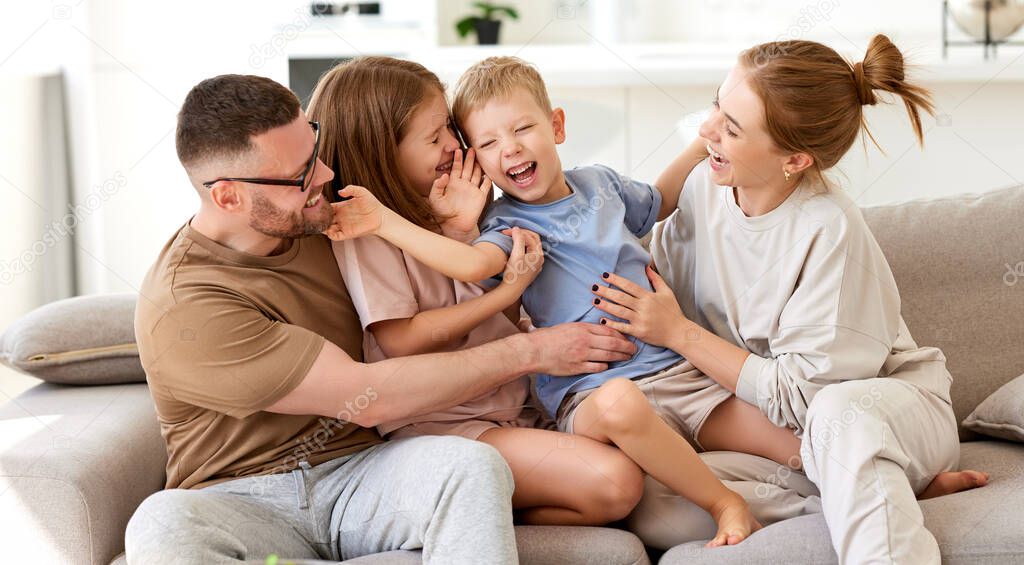 Happy family, young parents with two cute excited children son and daughter having fun, embracing and playing together while relaxing on sofa at home. Mom, dad and kids enjoying leisure time