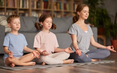 İki sakin çocuk nilüfer çiçekli erkek ve kız kardeş anne ile evde otururken gözlerini kapatıp meditasyon yapıyorlar. Anne çocuklara nasıl meditasyon yapılacağını öğretiyor.