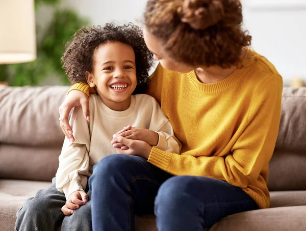 I love you, mom. Happy african american child son holding mothers hand, looking at camera and smiling while sitting together on sofa in living room. Young family mom and kid enjoying time together at home