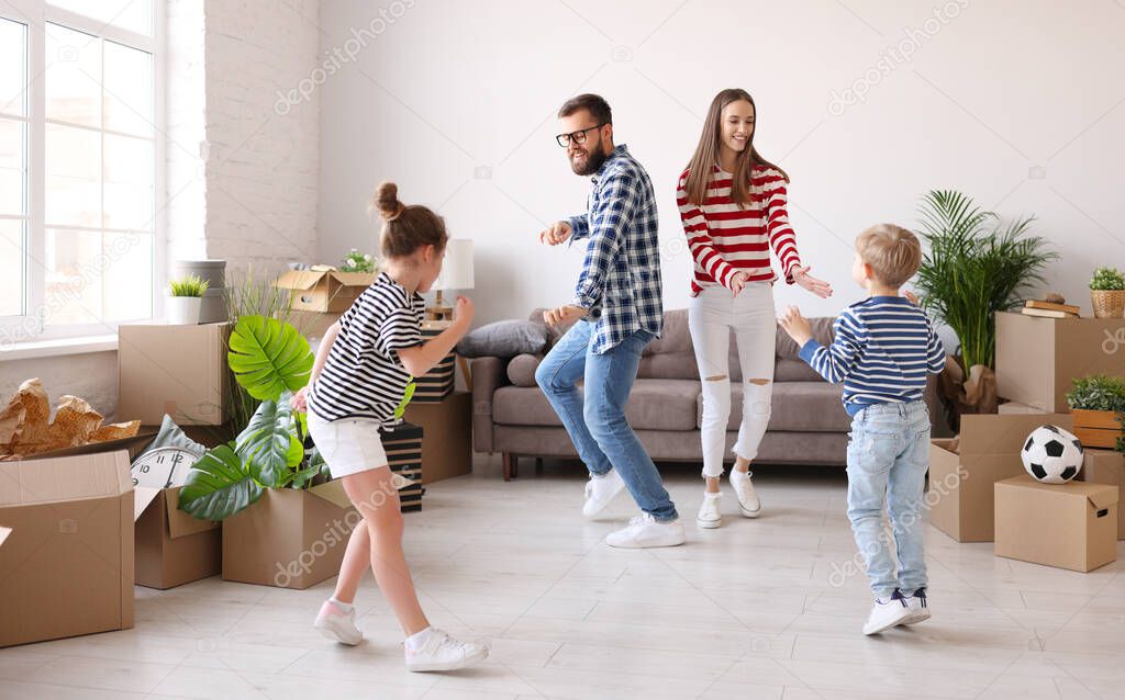 Full body family: mother and father   dancing with daughter and son near couch and carton boxes with belongings in new 