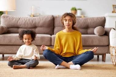 Çocuklu yoga. Genç Afro-Amerikan aile annesi ve küçük oğlu evde oturma odasındaki kanepede otururken gözleri kapalı meditasyon yapıyorlar.