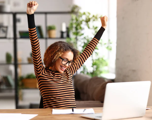 Excited afro american teenage girl   listening her favourite playlist while studying online on laptop, happy mixed race female celebrating success while working remotely from home