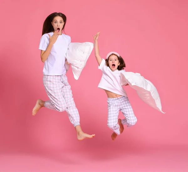 一个乐观的年轻女人和女孩 早上抱着枕头 在粉色的背景下跳起来 — 图库照片