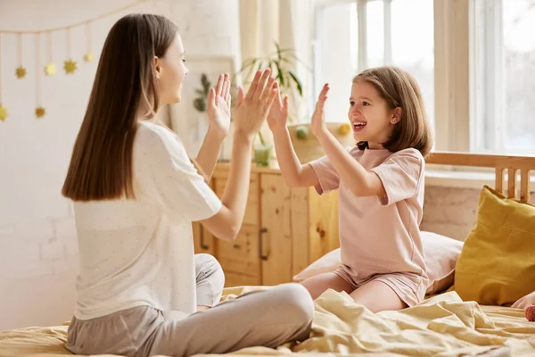 Aileyle eğleniyorum. Kafkasyalı iki kız, genç ve büyük mutlu kız kardeşler, sabahları yatakta otururken pijamalarıyla oynuyorlar, genç anne ve tatlı küçük kız evde eğleniyorlar.