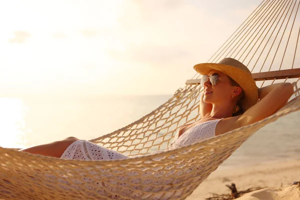 好好享受暑假吧年轻而快乐的女人 戴着草帽和太阳镜 在夕阳西下躺在沙滩上的吊床上 眼睛紧闭着 很放松 人们旅行的概念 — 图库照片