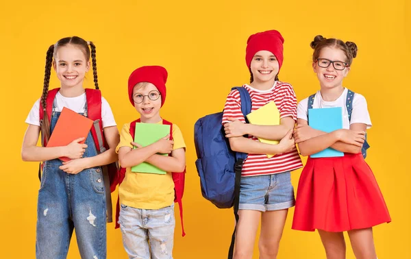 バックパックをカメラを見ながら黄色の背景を背景に一緒に立っているとカジュアルな服で楽観的な小学生のクラスメート — ストック写真