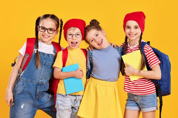 İyimser ilkokul öğrencileri sırt çantalı ve sarı arka planda yan yana dururken kameraya bakan gündelik giysiler içinde sınıf arkadaşları.