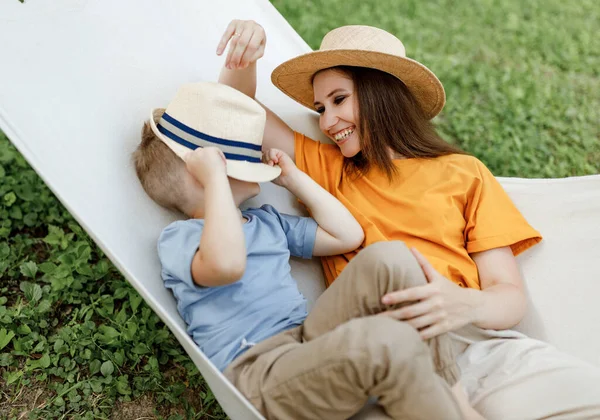 幸せな家族の母親と子供の息子は自然界の夏の庭でハンモックでリラックスしながら一緒に笑って遊ぶ — ストック写真