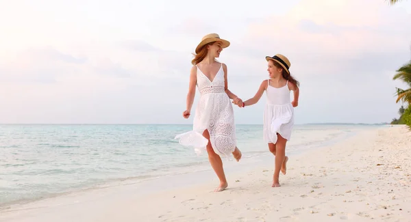 乐观的家庭 在阳光灿烂的日子里 穿着白衣的妇女和女孩手牵手 面带微笑地互相望着 在海边的沙滩上奔跑 — 图库照片