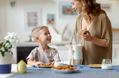 Memnuniyetle gülümseyen ve neşeli çocuk için taze süt döken bir kadın.
