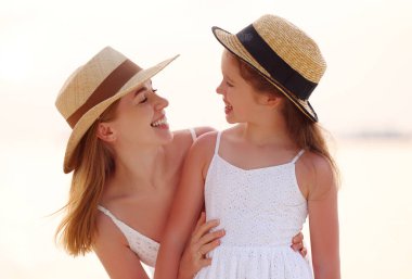 Mutlu kadın sarılıyor ve neşeli kıza bakıyor. Bulanık arka planda güneşli gökyüzü ve deniz tatil köyünde.