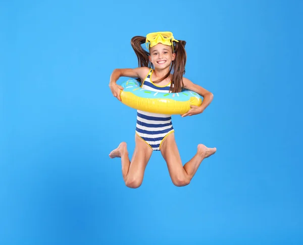 穿着泳衣 头戴护目镜的可爱的小女孩跳起来 腰围着充气环 与蓝色的工作室背景隔离在一起 假期和学校假期的概念 — 图库照片