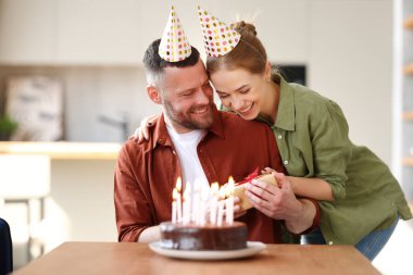 Genç, pozitif bir eş kocaya sürpriz yapıyor. Elinde hediye kutusu olan heyecanlı bir adam. Mutfakta pasta yerken çok mutlu. Parti şapkalı bir çift evde doğum günü kutluyor.