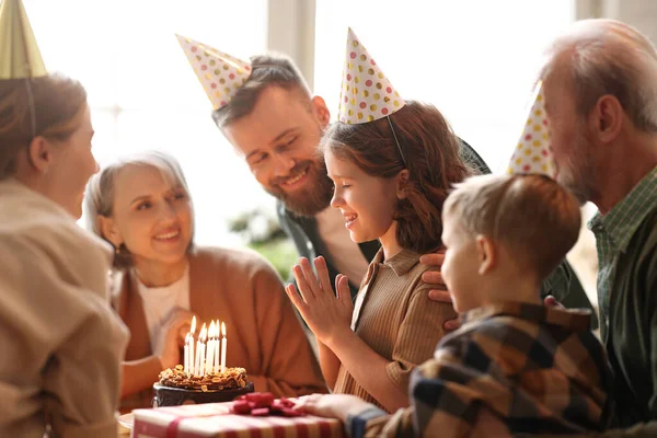 パーティーの帽子の中で幸せな大きな美しい家族は 家で小さな女の子の誕生日を祝いながら笑顔 ケーキにキャンドルを吹いてプレゼントを受け取る前に願いを作りながら興奮しているかわいい子供を感じます — ストック写真
