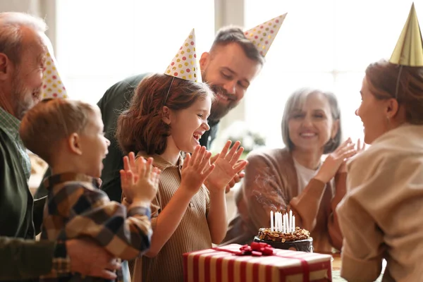 パーティーの帽子で幸せな大きな美しい家族は 家で小さな女の子の誕生日を祝いながら手を拍手と笑顔 ケーキの上にろうそくを吹き上げ プレゼントを受け取ると興奮したかわいい子供の気持ち — ストック写真