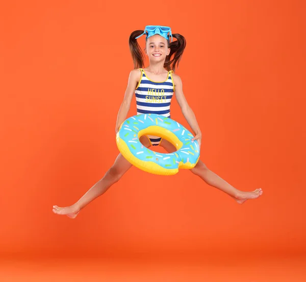 穿着泳衣 头戴护目镜的可爱的小女孩跳起来 腰围着充气环 与橙色工作室的背景隔离在一起 假期和学校假期的概念 — 图库照片