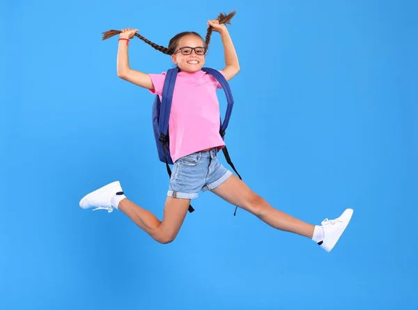 Hurry up to go back to school. Full length photo of energetic schoolgirl in eyewear with funny surprised facial expression captured in mid air, jumping from happiness and joy on blue studio background