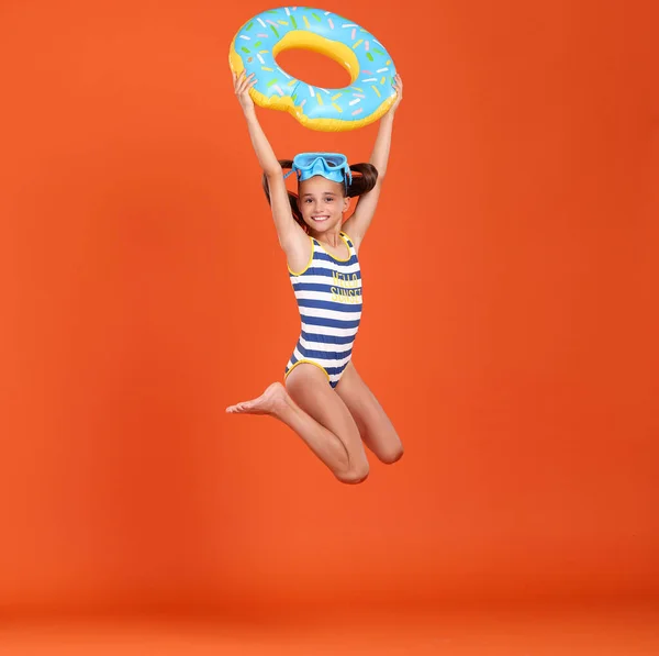 穿着泳衣 头戴护目镜的可爱的小女孩跳起来 腰围着充气环 与橙色工作室的背景隔离在一起 假期和学校假期的概念 — 图库照片