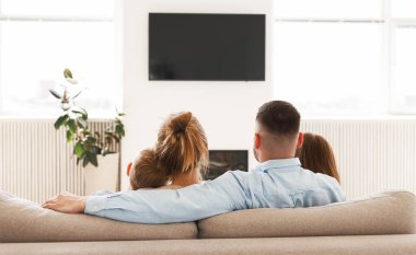 Genç aile, baba, anne ve iki küçük çocuğun şöminenin önünde oturup televizyon izlemesi, bağ kurması ve evde vakit geçirmenin keyfini çıkarması.