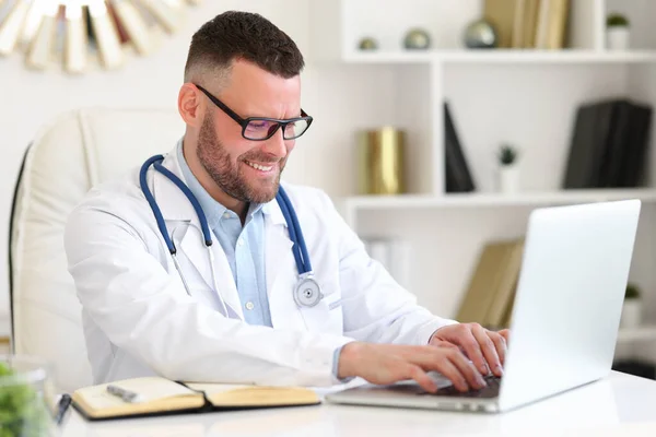 Wesoły Przyjazny Lekarz Białym Płaszczu Stetoskopem Ramionach Patrzący Uśmiechem Laptopa — Zdjęcie stockowe