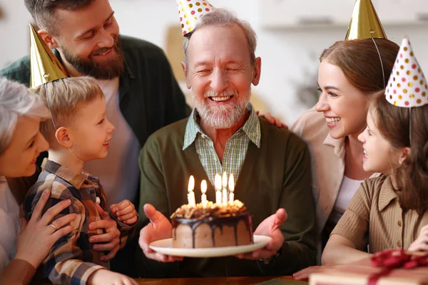 祖父の誕生日を祝うパーティー帽子を身に着けている幸せな大白人家族室内で 幸せな高齢者のおじいちゃんは家でお祝いの間にお祝いを受け ろうそくでケーキを保持 — ストック写真