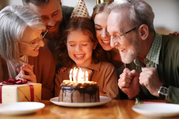 可愛いです興奮した小さな子供作る願いと家で幸せな女の子を祝うパーティー帽子の大きな美しい家族 正の両親と祖父母と誕生日を祝いながら ケーキの上にキャンドルを吹いて — ストック写真