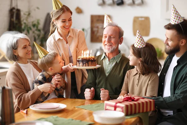 祖父の誕生日を祝うパーティー帽子を身に着けている幸せな大白人家族室内で 幸せな高齢者のおじいちゃんは家でお祝いの間にお祝いを受け ろうそくでケーキを保持 — ストック写真