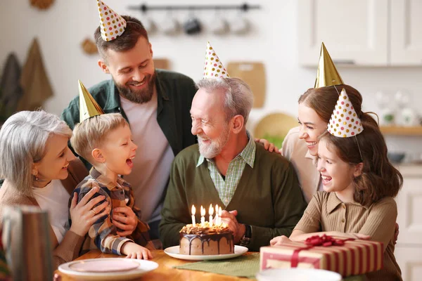 祖父の誕生日を祝うパーティー帽子を身に着けている幸せな大白人家族室内で 幸せな高齢者のおじいちゃんは家でお祝いの間にお祝いを受け ろうそくでケーキを保持 — ストック写真