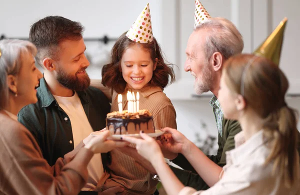 かわいいです興奮した小さな女の子作る願いとケーキの上にキャンドルを吹いている間お祝いの誕生日で大きな美しい家族 正の両親と祖父母でパーティー帽子お祝いの幸せな女の子自宅 — ストック写真