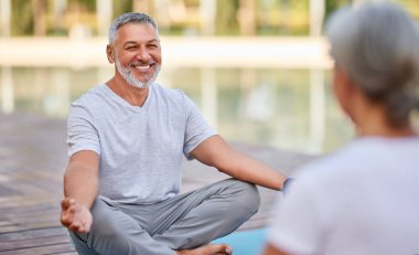 Mutlu, olgun bir adam yoga nilüferinde oturmuş elleri Mudra jesti ile poz veriyor ve sabah meditasyonu sırasında karısıyla parkta temiz hava alırken gülümsüyor son sınıf aile çifti dışarıda meditasyon yapıyor.