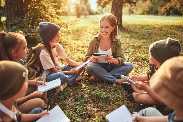 Schoolactiviteiten Natuur Groep Nieuwsgierige Kinderen Jonge Vrouwelijke Leerkracht Zitten Samen — Stockfoto