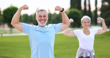 Fit yaşlı çift dışarıda çalışıyor. Kollarını açıp kaslarını gösteriyor. Kameraya bakıyor ve gülümsüyor, olumlu karı koca açık havada sabah fiziksel aktivitelerinin keyfini çıkarıyor.