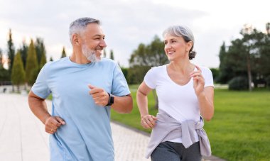 Şehir parkında spor kıyafetleriyle koşan mutlu kıdemli karı koca güneşli bir sabah koşan sevimli emekliler birbirlerine sıcakkanlılıkla ve gülümseyerek bakıyorlar. Sağlıklı yaşam tarzı kavramı