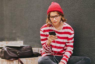 Gözlüklü, komik kıyafetli, kulaklıklı, okul çantalı, paket kahveli, cep telefonlu arkadaşlarıyla mesajlaşan, internette sınıf arkadaşlarıyla sohbet eden huysuz öğrenci portresi.