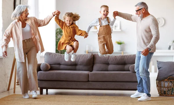 快乐的祖父母和孙子孙女们周末在客厅里玩乐玩耍 精力充沛的老奶奶和爷爷牵着孩子们的手从沙发上跳起来 — 图库照片