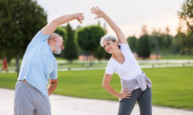 Sağlıklı zihin ve vücut. Güneşli bir sabahta parkta birlikte ısınırken spor giyim kuşamında gülümseyen olgun aile babası ve kadın kollarını esnetiyorlar. Etkin yaşam biçimi
