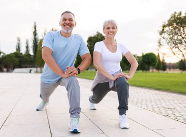 Energize your morning. Full length of active happy elderly family couple in sportswear working out together in city park in morning. Joyful senior husband and wife making sport outdoors, warming up clipart