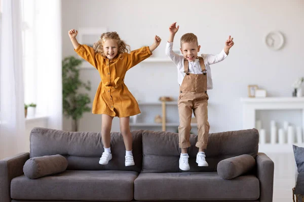 기쁨에 넘치는 자녀들 소파에서 뛰어오르는 아이들 집에서 놀면서 재미있게 아이들 — 스톡 사진