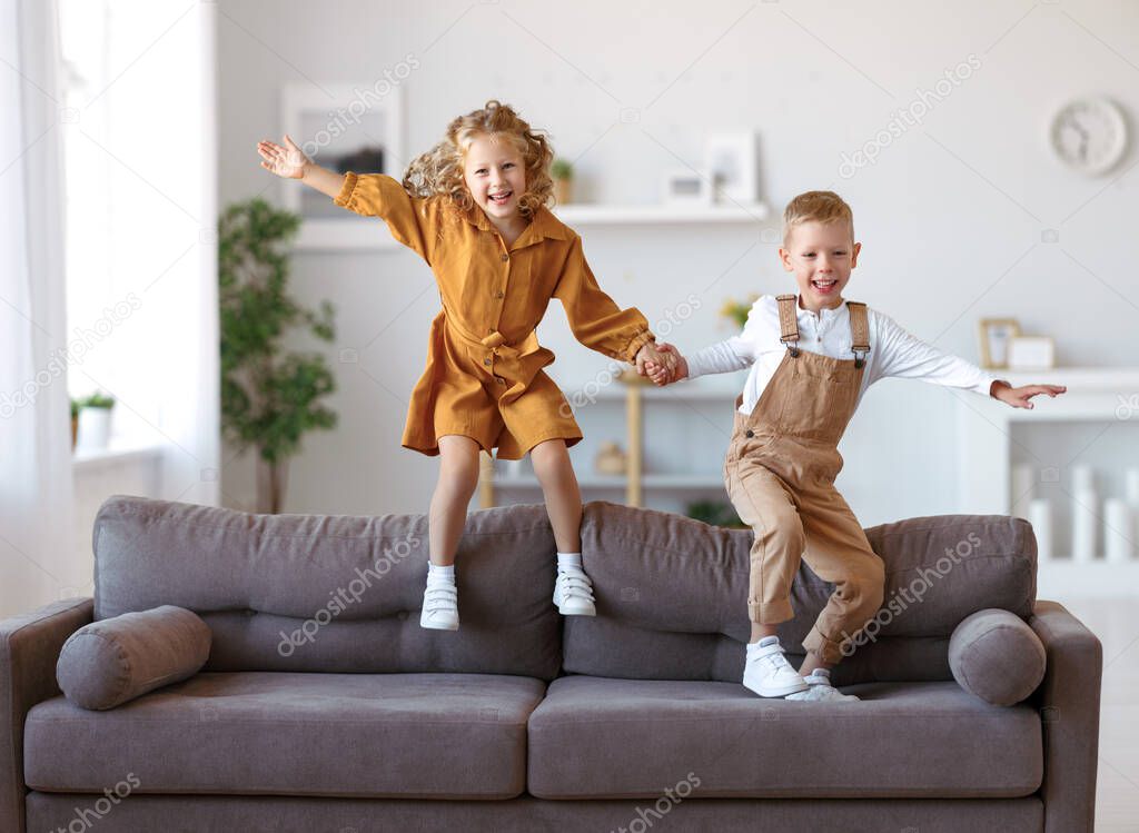 Full length of overjoyed little children brother and sister jumping on sofa, laughing and having fun while playing together at home, kids enjoying carefree leisure time at home