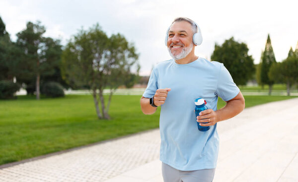 Hombre Maduro Feliz Auriculares Sosteniendo Botella Agua Mientras Trota Afuera — Foto de Stock