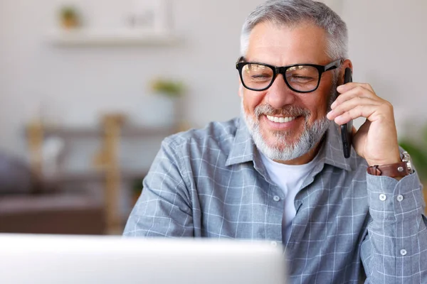 Przystojny Starszy Pan Okularach Rozmawiający Przez Telefon Komórkowy Patrzący Laptopa — Zdjęcie stockowe