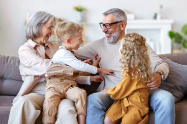 Oyuncak çocuklar ve büyükanneler evde eğlenirken büyükbabalarını gıdıklıyor, mutlu aile büyükbabaları ve çocukları birlikte eğleniyor ve oturma odasındaki kanepede dinlenirken oyun oynuyorlar.